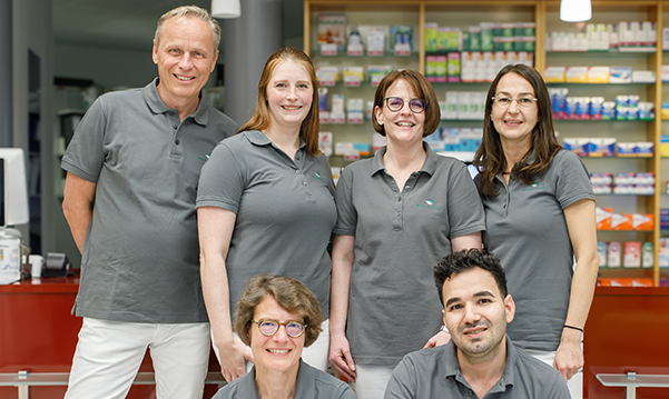 Team und Inhaber der Trierweiler Apotheke in Trierweiler stehen in der Apotheke für ein Gruppenfoto zusammen.