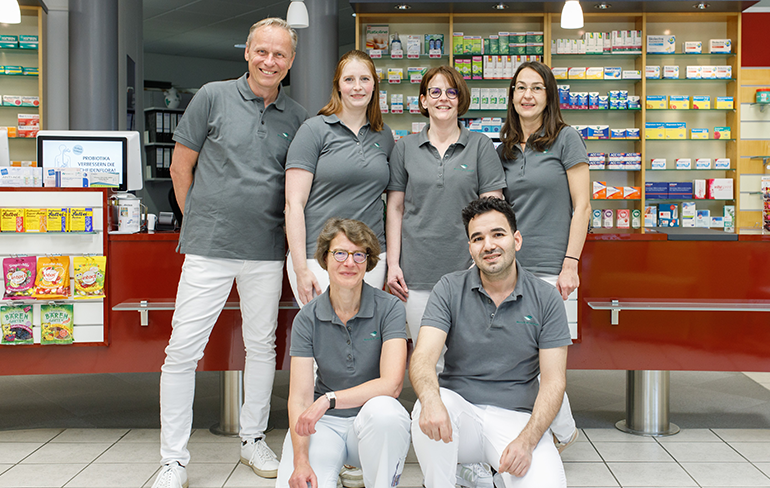 Team und Inhaber der Trierweiler Apotheke in Trierweiler stehen in der Apotheke für ein Gruppenfoto zusammen.