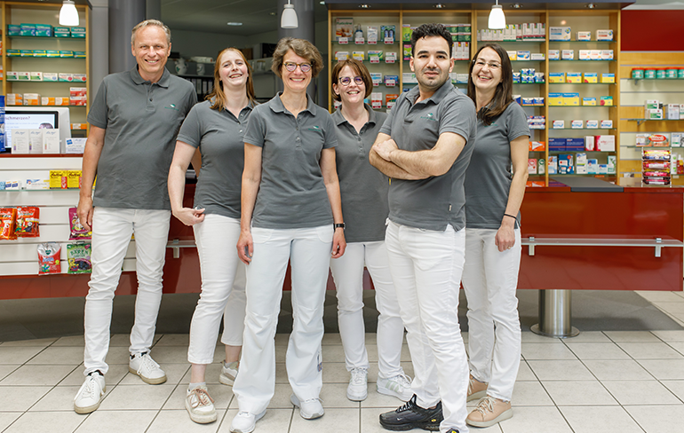 Team und Inhaber der Trierweiler Apotheke in Trierweiler stehen in der Apotheke für ein Gruppenfoto zusammen.