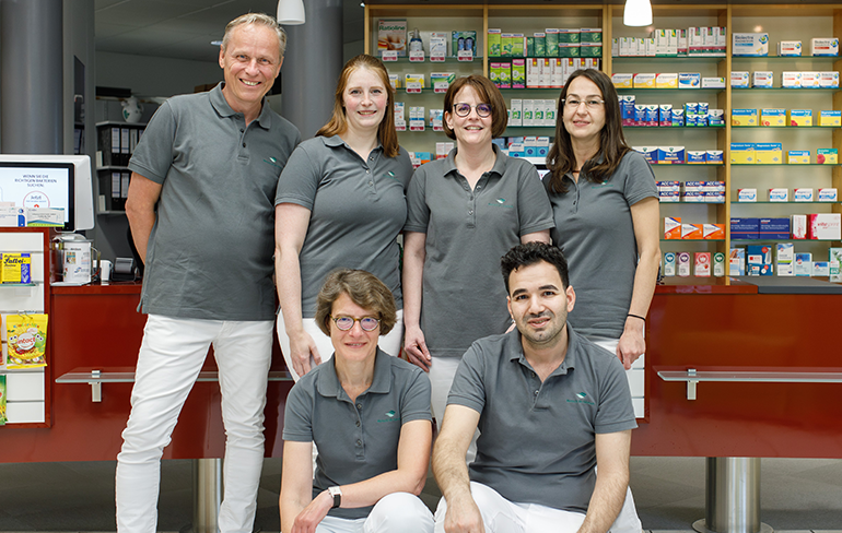 Team und Inhaber der Trierweiler Apotheke in Trierweiler stehen in der Apotheke für ein Gruppenfoto zusammen.