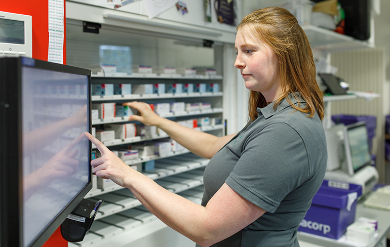 Apothekerin der Trierweiler Apotheke steht am Monitor und holt ein Medikament aus dem Regal.