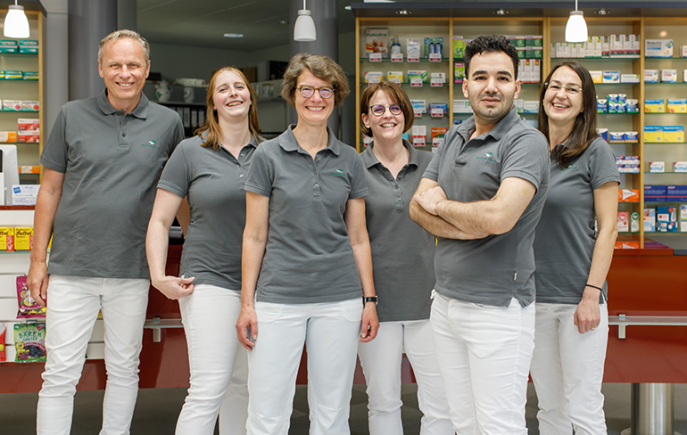 Team und Inhaber der Trierweiler Apotheke in Trierweiler stehen in der Apotheke für ein Gruppenfoto zusammen.