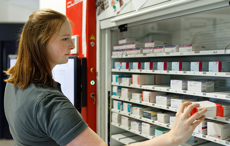 Apothekerin der Trierweiler Apotheke steht am Medikamentenregal und holt ein Medikament aus dem Regal.