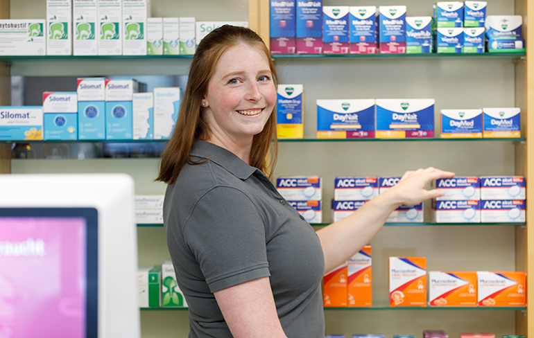 Apothekerin der Trierweiler Apotheke steht vor einem Medikamentenregal und greift nach einem Medikament.