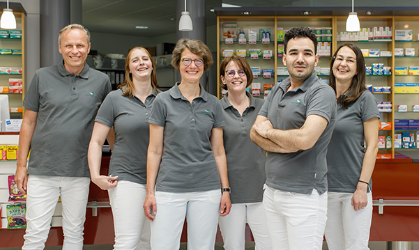 Team und Inhaber der Trierweiler Apotheke in Trierweiler stehen in der Apotheke für ein Gruppenfoto zusammen.
